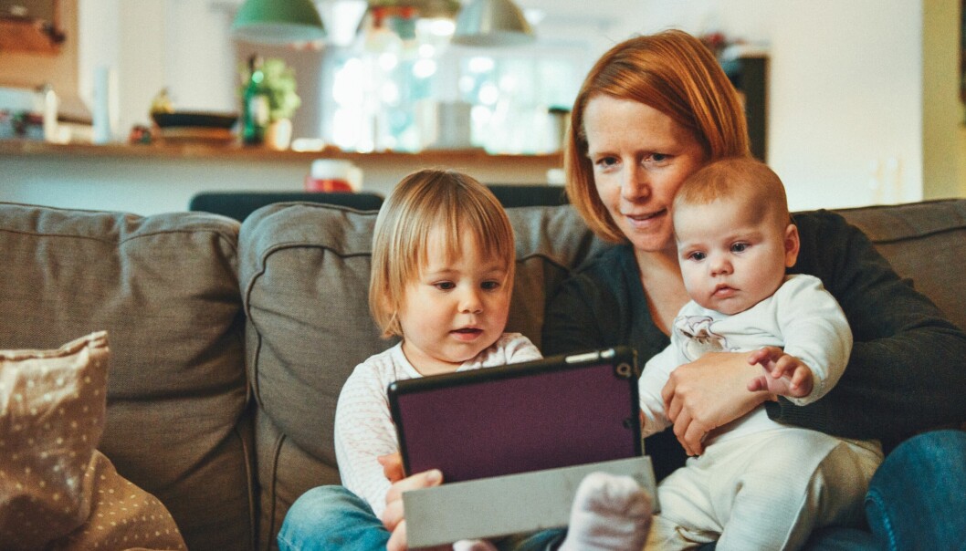 En mamma sitter i soffan med sina två barn och tittar på en Ipad.
