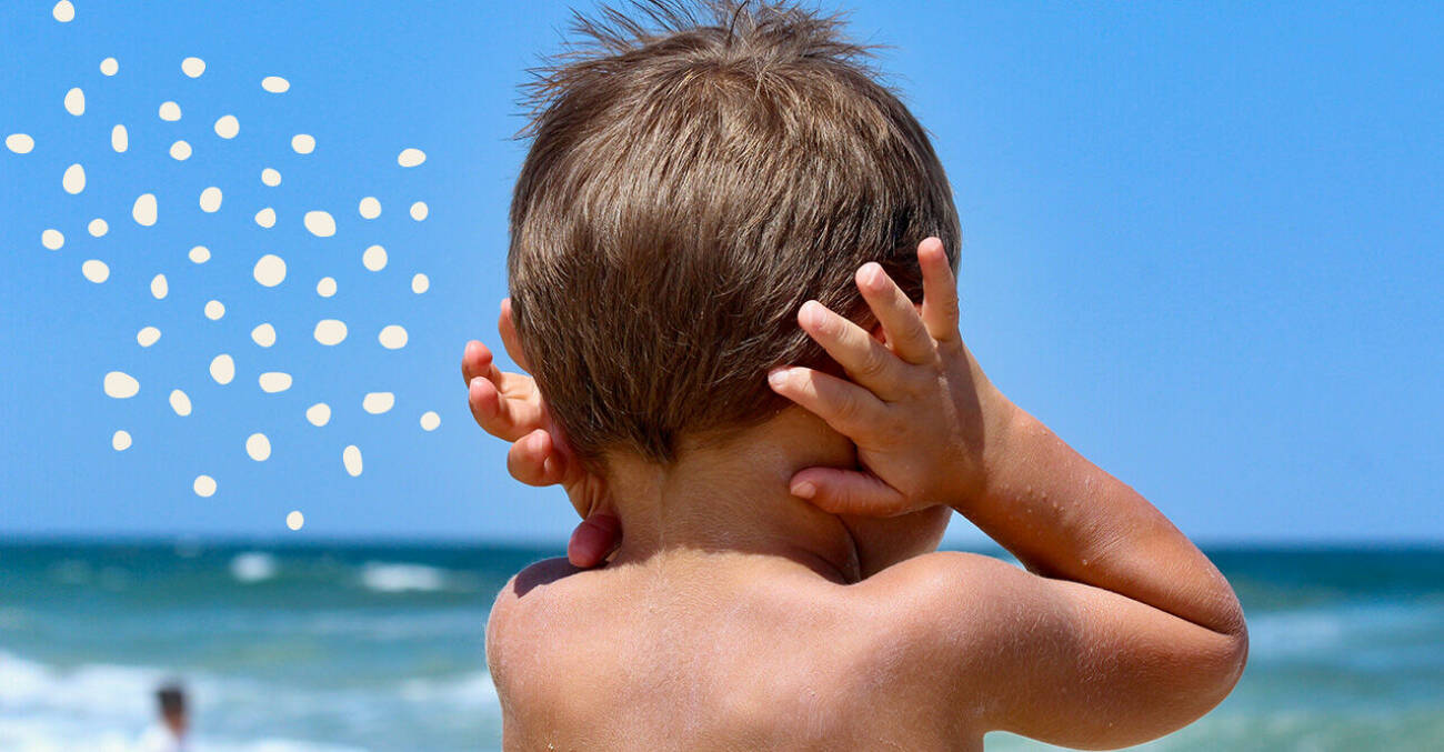 Litet barn på stranden som håller sig för öronen.