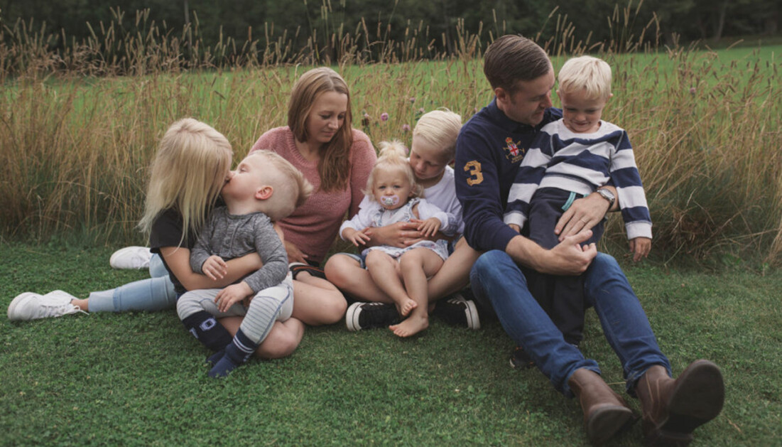 Familjen Bromander Sandén. Malin och hennes make Calle sitter vid en äng med fem barn.