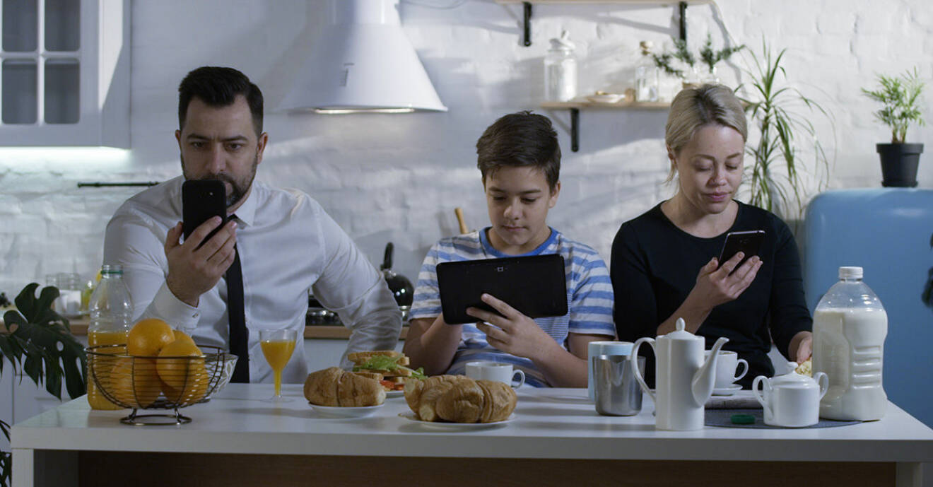 Familj med smartphones vid matbordet.