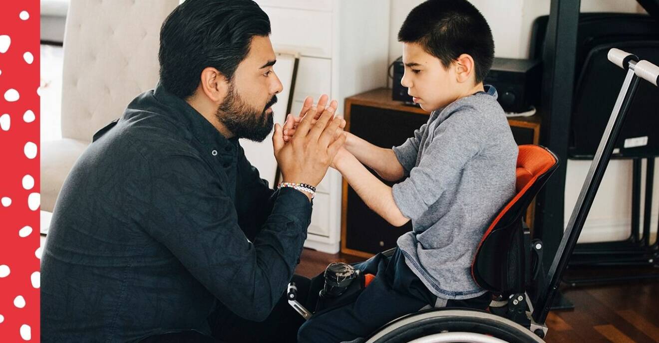 Pojke i rullstol håller hand med sin pappa.