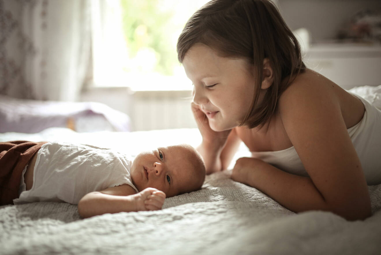storasyster och bebis på sängen
