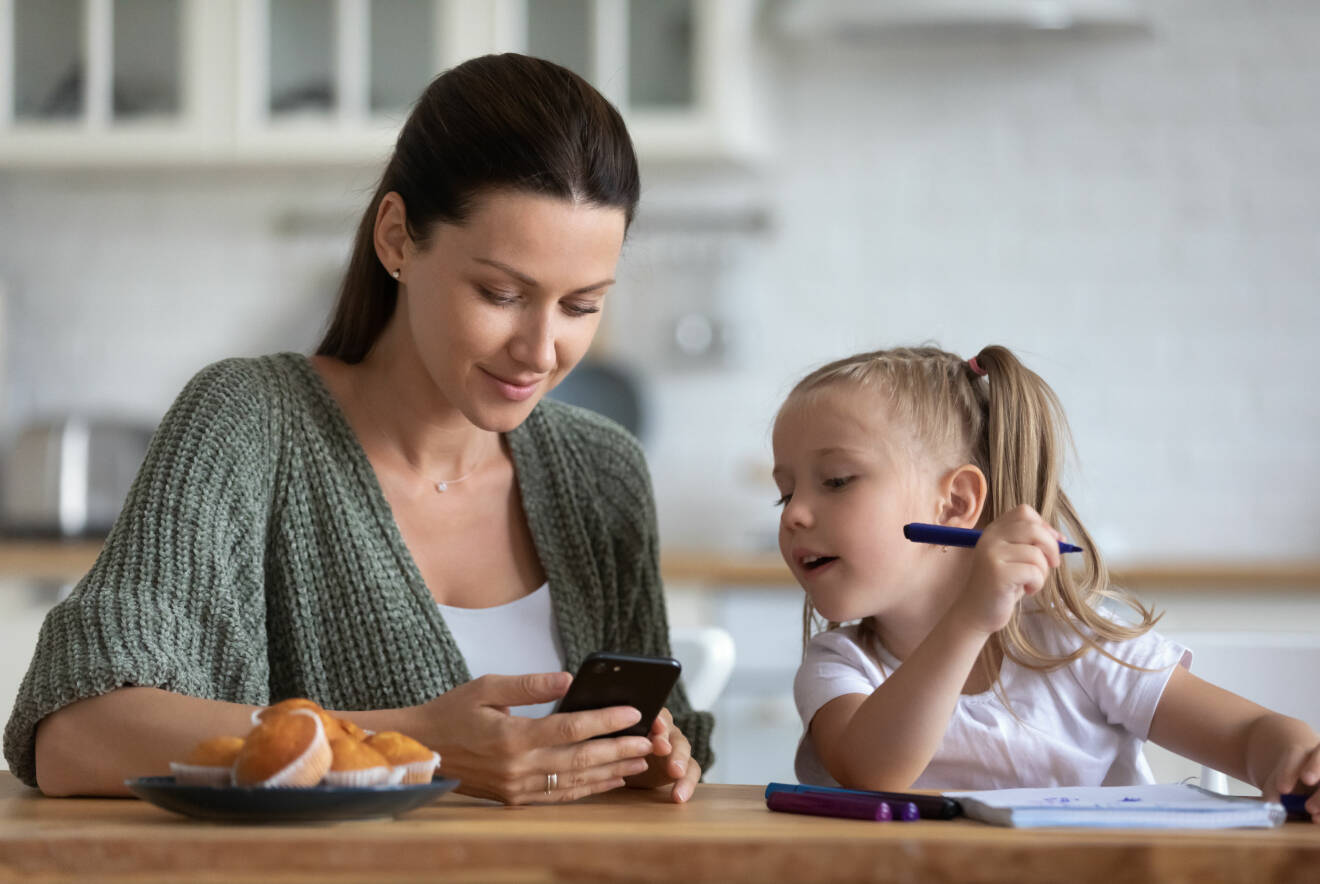 mamma och barn vid matbordet med mobiltelefon