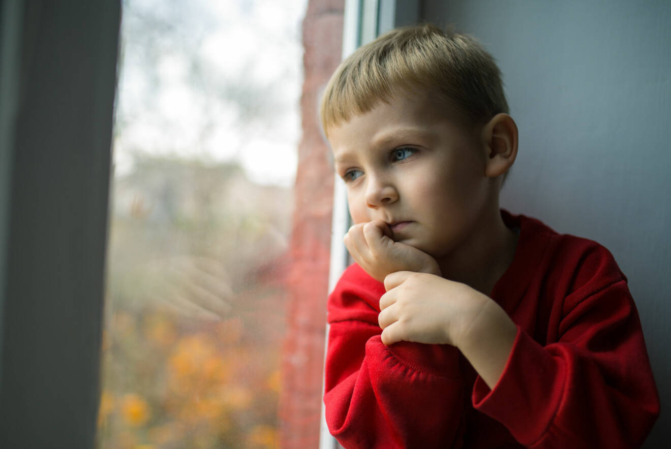 liten pojke som tittar ut genom ett fönster och är ledsen