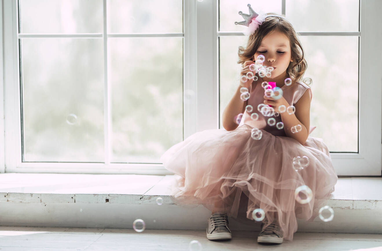 Flicka sitter i klänning och blåser bubblor