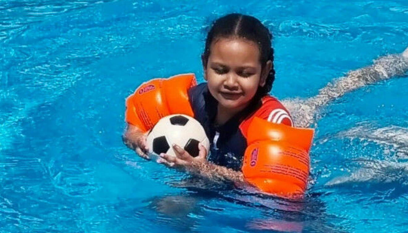 Ellie simmar i en pool och håller en fotboll i famnen.