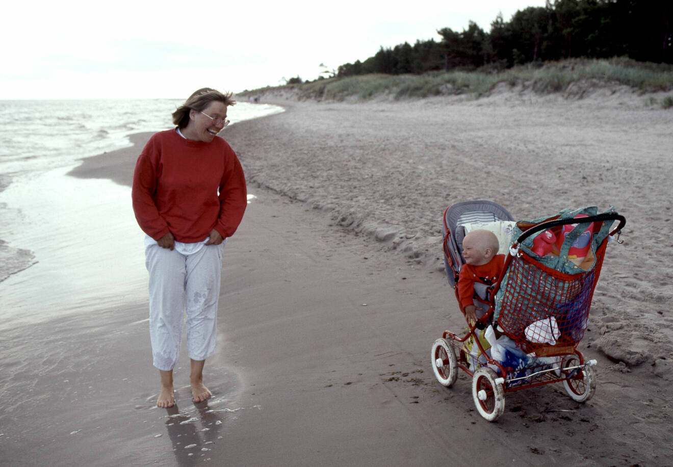 mamma står på stranden med sitt barn i barnvagnen