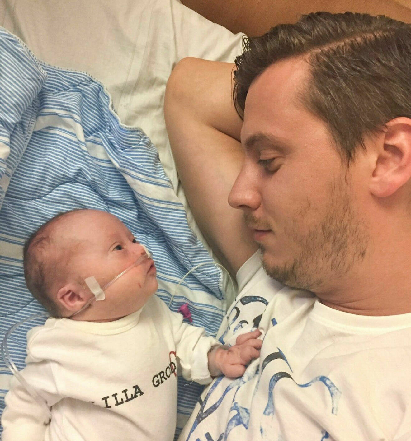 Nyfödde Svante och pappa Patrik ligger i en sjukhussäng och tittar på varandra.