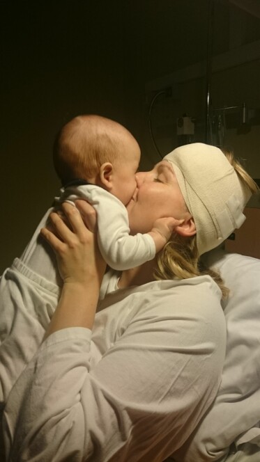 Maja har bandage runt huvudet och håller sin nyfödda son.