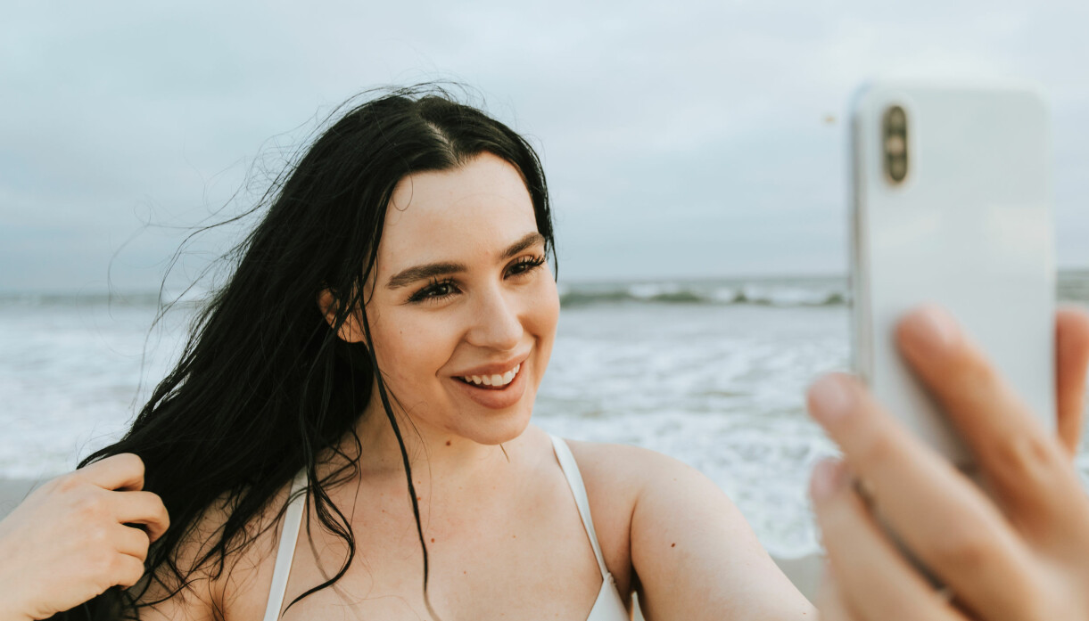 Att känna sig extra hungrig eller trött är vanligt i början av en graviditet. Kvinna är på stranden och tar selfie